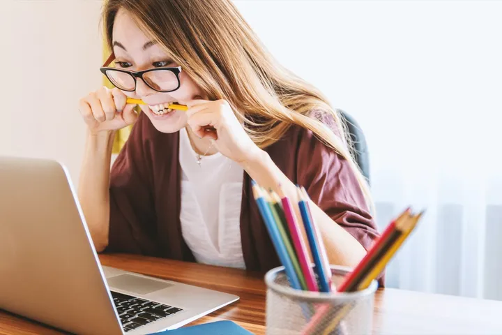 Femme stressée mordillant un crayon devant son ordinateur